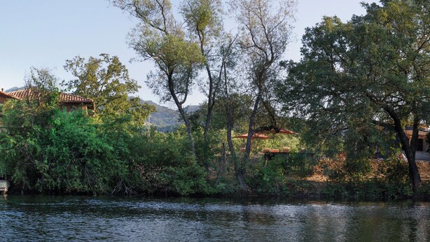 A lakeside property with a bridge connecting two buildings, surrounded by trees and a calm lake.