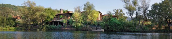 A lakeside property with a bridge connecting two buildings, surrounded by trees and a calm lake.