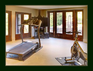 A home gym with a treadmill and stationary bike, large windows, and a view of the outdoors.