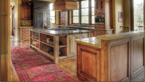 Une cuisine spacieuse avec des meubles en bois, un grand îlot central et un tapis rouge à motifs.