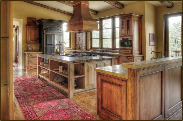 A spacious kitchen with wooden cabinets, a large island, and a red patterned rug.