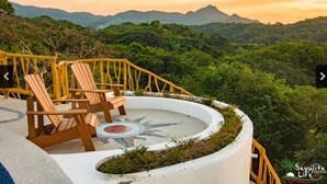 Una terraza con sillas de madera y un piso de mosaico circular, con vistas a un paisaje exuberante y montañas.