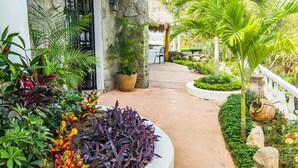 Un sendero en un jardín tropical que conduce a un edificio con fachada de piedra y techo de paja.
