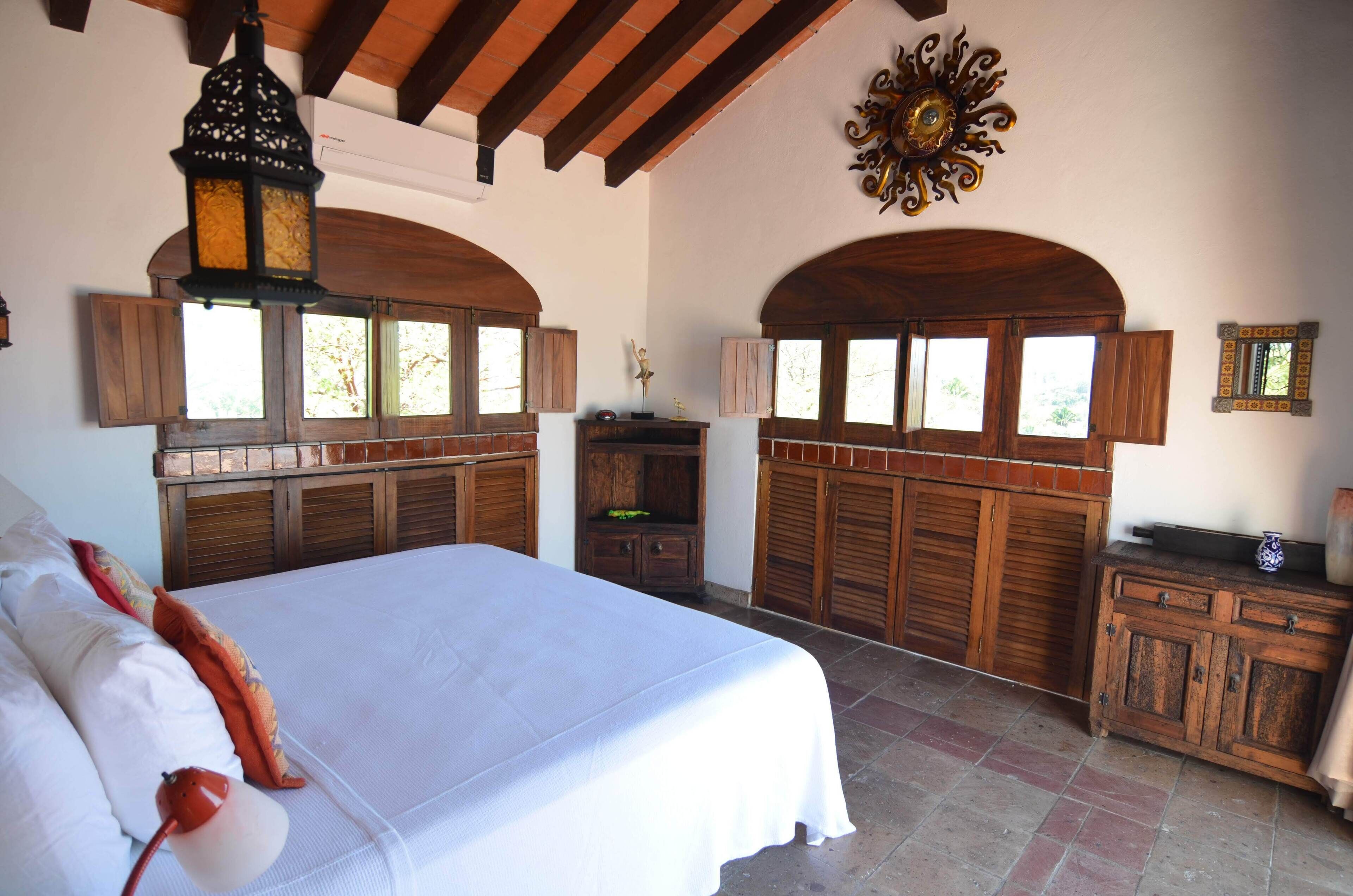 Un dormitorio con una cama grande, armarios de madera y ventanas arqueadas.