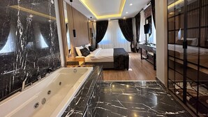 A modern hotel room with a large marble bathtub, a neatly made bed, a small bedside table, and a large mirror. - Kaya Life Resort (Çaykara)