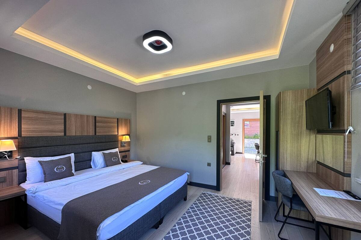 A modern hotel room with a large bed, bedside tables with lamps, a desk, and a TV mounted on the wall.