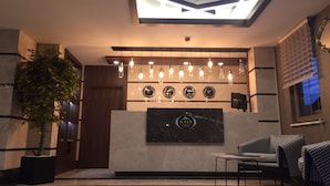 A reception area with a modern ceiling design, a reception desk with a logo, and seating arrangements. - Kaya Life Resort (Çaykara)