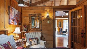 A cozy wooden room with a bed, a chair, a mirror, and a door leading to another room. - Walk Softly, There’s a Dream Here! (Colchester)