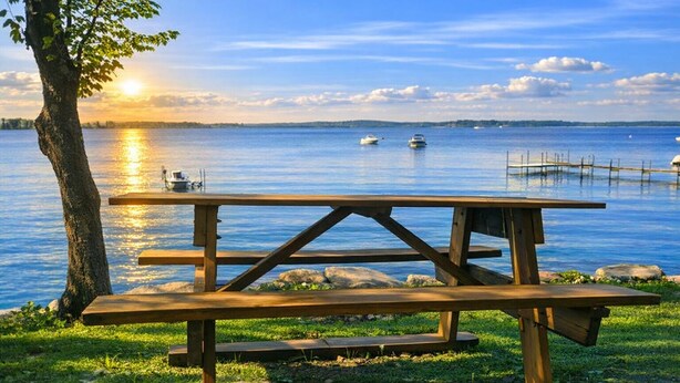 A wooden picnic table by a lake with boats in the background. - Walk Softly, There’s a Dream Here! (Colchester)