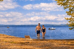A couple walking by a lake with a boat and a chair on the shore.