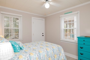 A bedroom with a bed, two windows with blinds, a ceiling fan, and a turquoise dresser. - Bill's Place: Dog-Friendly with Fenced Yard One Block from the Beach (Oak Island)