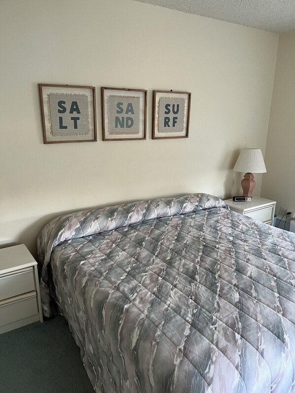 Un dormitorio con una cama, una mesita de noche, una lámpara y tres carteles enmarcados en la pared.