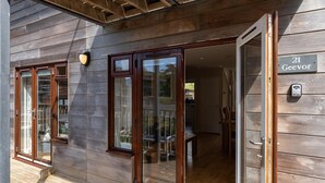 A wooden building with a sliding glass door, a wooden deck, and a sign indicating the address. - Coastal eco-home for up to 6, short walk from Porthtowan village and beach (Porthtowan)