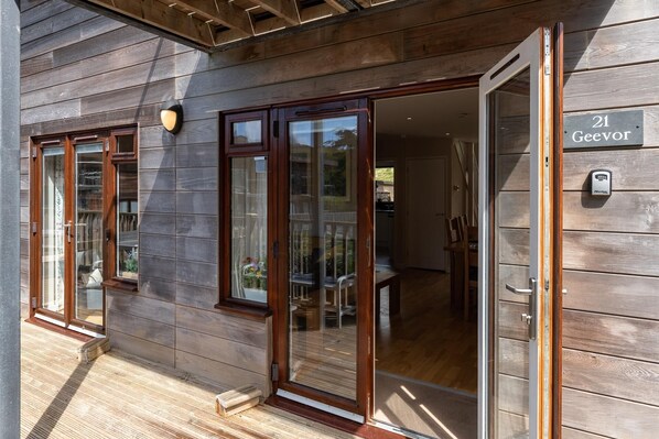 A wooden building with a sliding glass door, a wooden deck, and a sign indicating the address. - Coastal eco-home for up to 6, short walk from Porthtowan village and beach (Porthtowan)