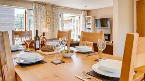 A dining area with a wooden table set for four, including wine glasses, plates, and cutlery. - Coastal eco-home for up to 6, short walk from Porthtowan village and beach (Porthtowan)