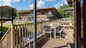A wooden deck with outdoor seating and a view of a wooden building with balconies. - Coastal eco-home for up to 6, short walk from Porthtowan village and beach (Porthtowan)