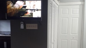 A room with a flat-screen TV mounted on a dark wall, a white door, and a black trash bin. - Exquisite, recently renovated studio apartment (New Kingston)