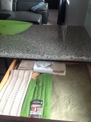 Uma área de cozinha com bancada de granito, uma gaveta com toalhas dobradas e um pano verde.