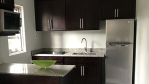 A modern kitchen with dark cabinets, a stainless steel refrigerator, a built-in microwave, and a granite countertop. - Exquisite, recently renovated studio apartment (New Kingston)