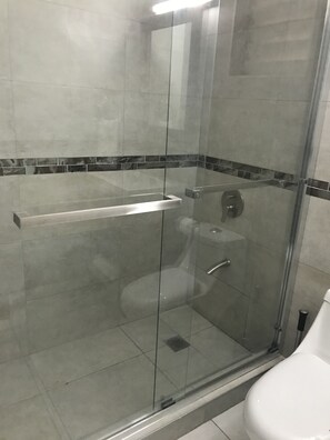 Divisória de chuveiro com vidro, vaso sanitário branco e piso ladrilhado.