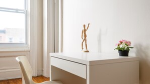 Ein weißer Schreibtisch mit einer Holzpuppe, einem weißen Stuhl und einem Blumentopf mit rosa Blüten.