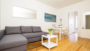 Ein modernes Wohnzimmer mit einem grauen Ecksofa, einem weißen Beistelltisch mit Blumenvase und einem Bild an der Wand.