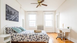 Ein Schlafzimmer mit Bett, Schreibtisch, Heizkörper und Deckenventilator.