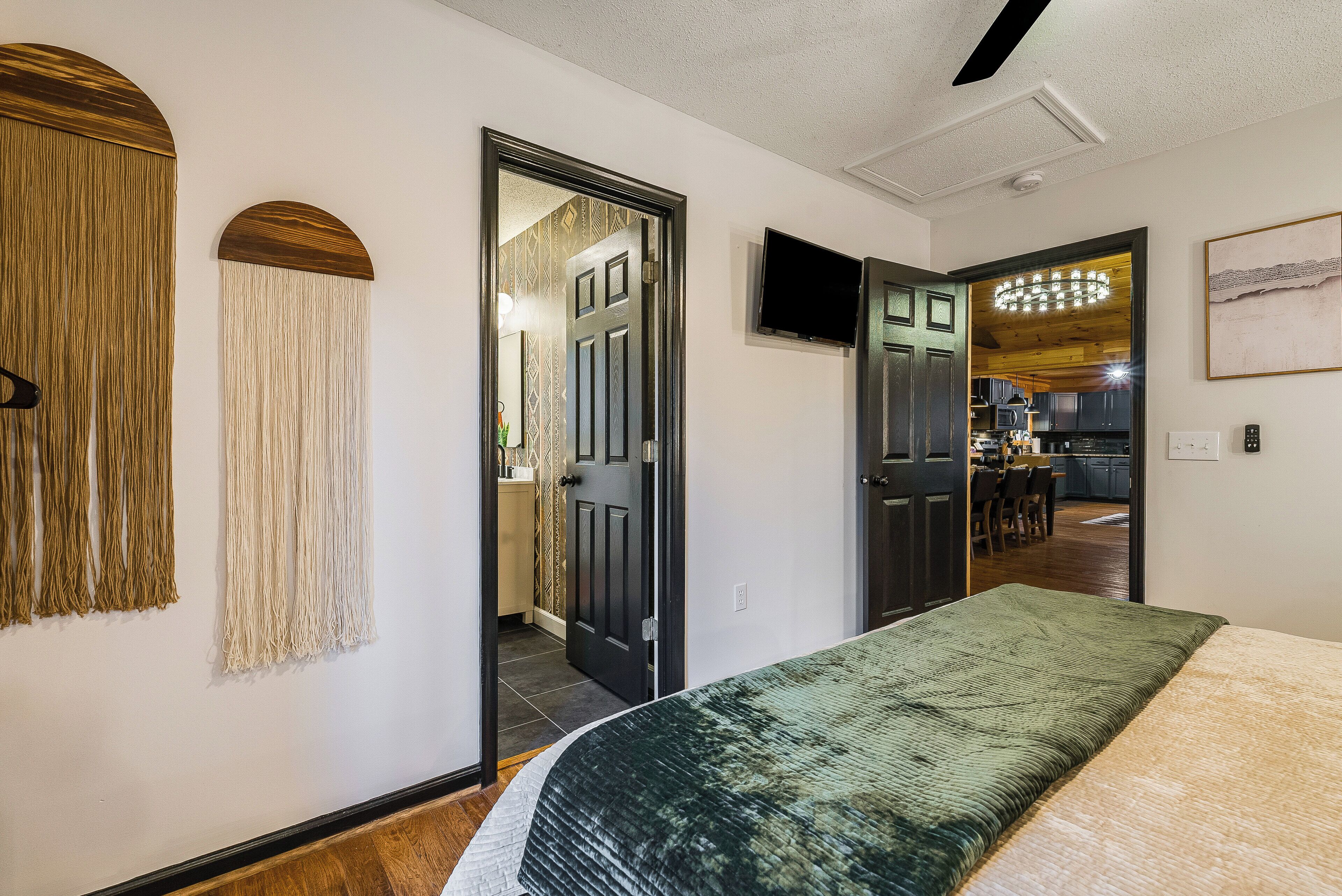 A bedroom with a bed, a TV, and a door leading to a kitchen.
