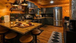Interior de una cabaña de madera con una isla de cocina, taburetes de bar y un refrigerador.