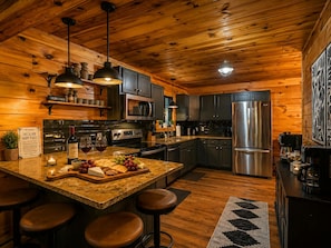 A wooden cabin interior with a kitchen island, bar stools, and a refrigerator.
