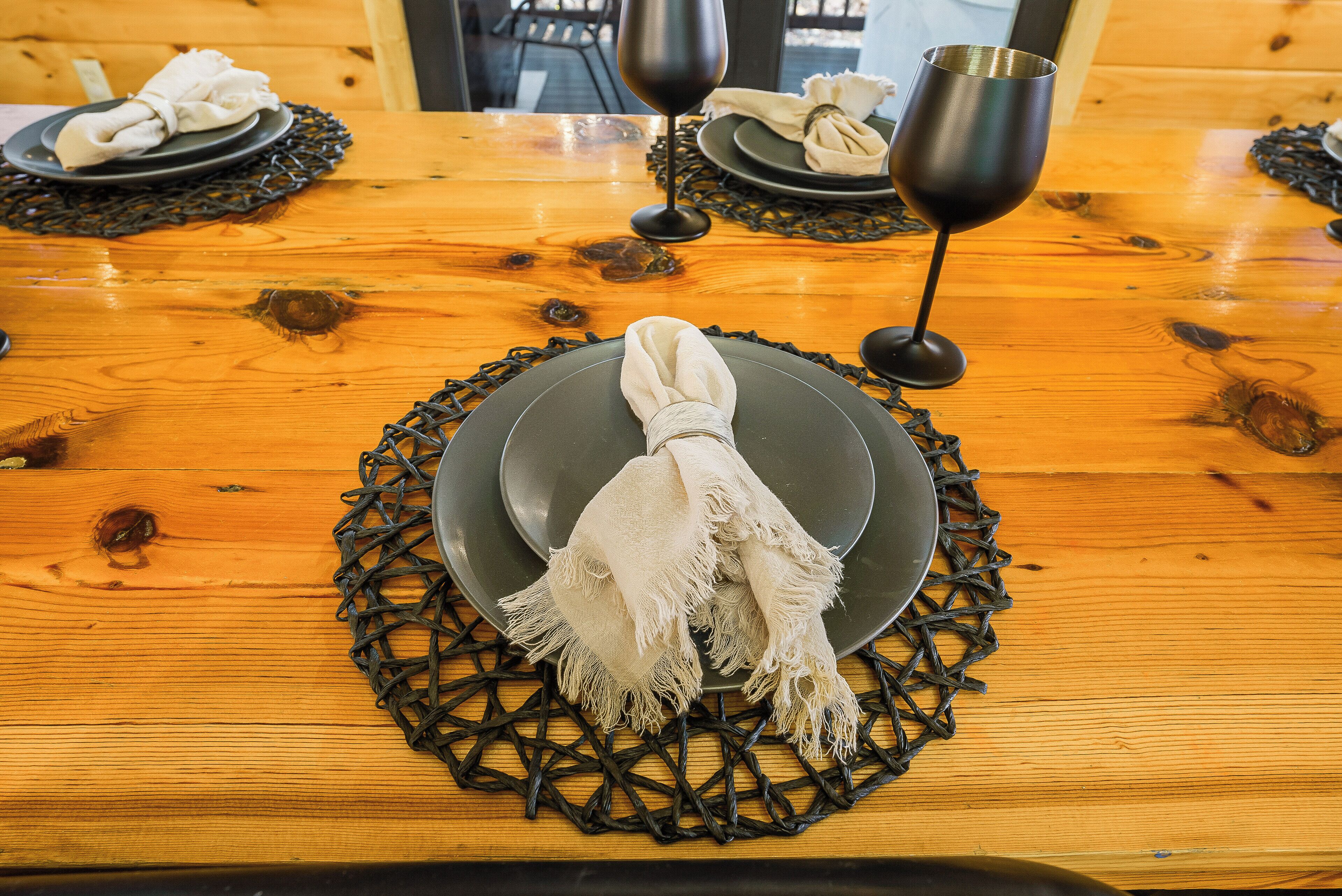 A wooden dining table with black placemats and a folded white napkin.