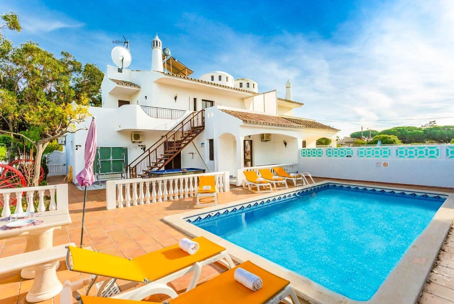 A white villa with a swimming pool, outdoor seating, and a staircase leading to a terrace.