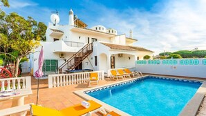 A white villa with a swimming pool, outdoor seating, and a staircase leading to a terrace.