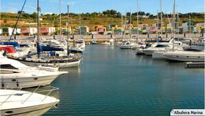 A marina with multiple boats docked, surrounded by colorful buildings and a clear sky.