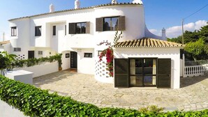 A white two-story house with a tiled roof, a small garden, and a paved courtyard.