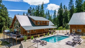 A wooden lodge with a pool, deck chairs, and a view of the forest.