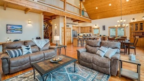 A spacious living area with a high ceiling, wooden beams, a dining area, and a kitchen.