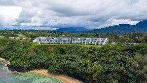 A resort with multiple buildings, a beach, and a mountainous backdrop. - Sapphire Lotus~Ocean Front~A/C~Pool~BBQ (Princeville)