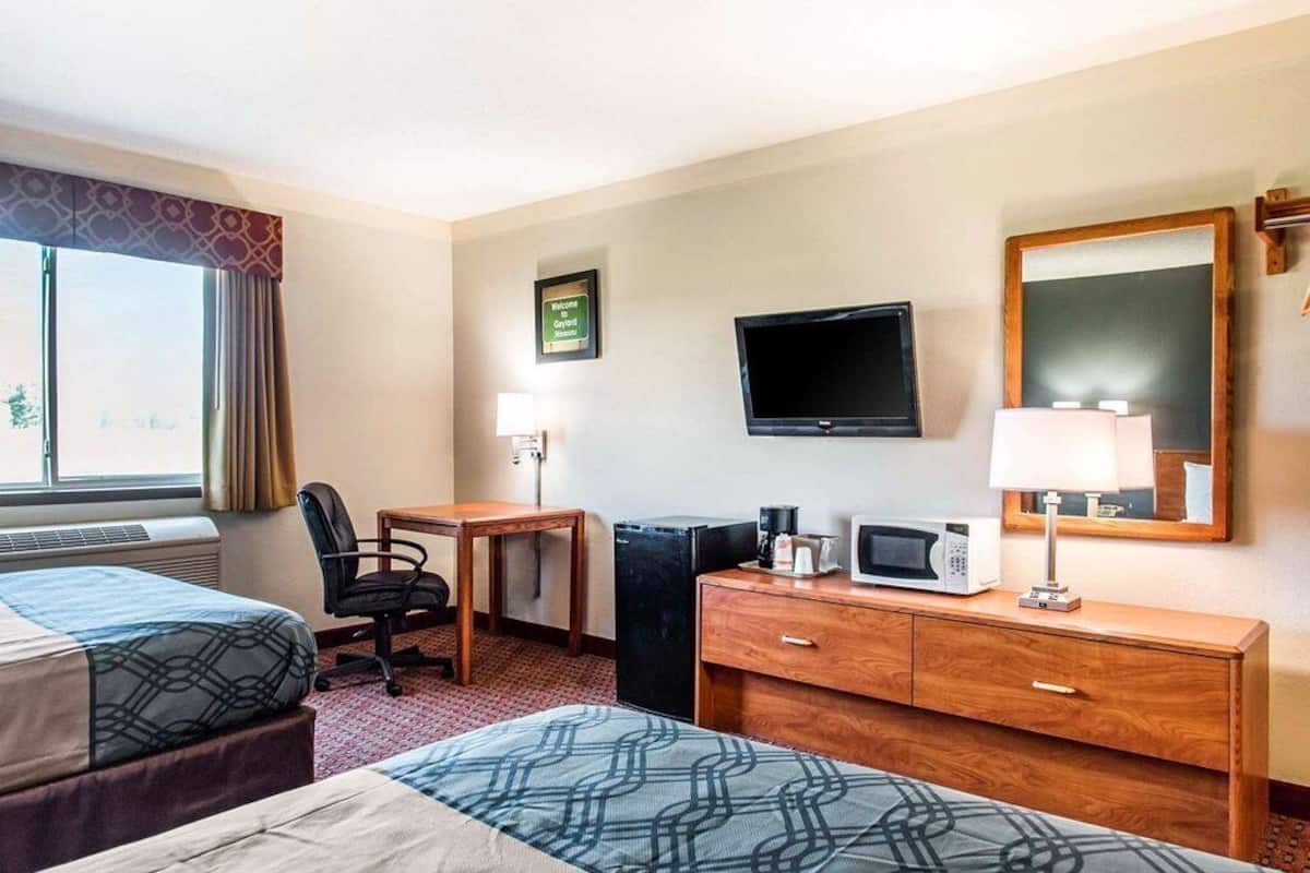 A hotel room with two beds, a desk, a television, a microwave, and a small refrigerator.