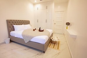 A bedroom with a large bed, a wardrobe, a small table with decorative items, and a vase with flowers on the wall. - K Building (Ho Chi Minh City)
