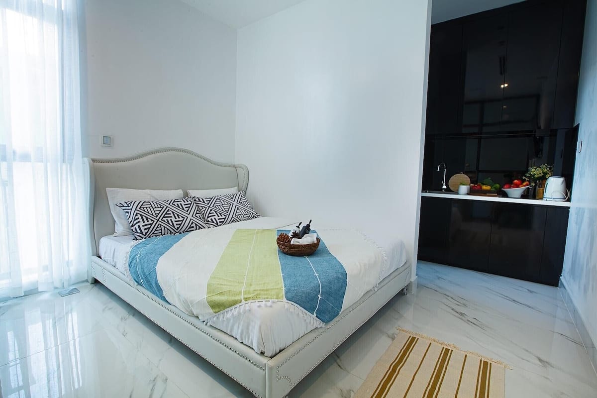 A modern bedroom with a white bed, patterned pillows, and a bedside table with a basket and a small statue.