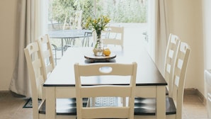Un comedor con una mesa, sillas, un ventilador de techo y una ventana con cortinas.