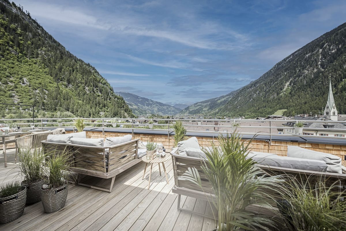 Una terraza en la azotea con mobiliario de madera, plantas en macetas y una vista panorámica de las montañas.