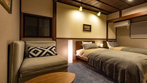 Una habitación acogedora con sofá, dos camas, una mesita de noche y aire acondicionado de pared.