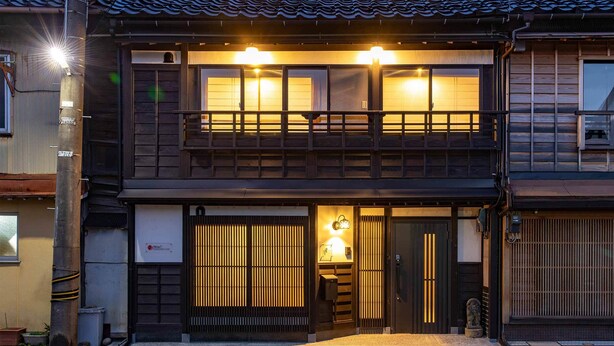 Un edificio tradicional japonés con fachada de madera, un balcón con barandilla y una puerta corredera con listones verticales.