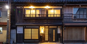 A traditional Japanese-style building with a wooden facade, a balcony with railings, and a sliding door with vertical slats.