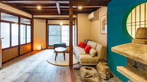 Una habitación tradicional japonesa con suelo de tatami, una mesa baja de tatami, un sofá con cojines y una escultura de piedra.