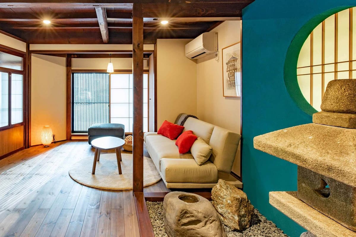 Habitació tradicional d'estil japonès amb sòl de tatami, una taula de tatami, un sofà amb coixins i una escultura de pedra.