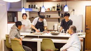 Una cocina moderna con una isla central, luces colgantes y un refrigerador con una botella de vino encima.