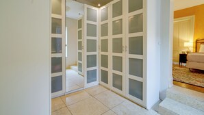 A hallway with a white door leading to a bedroom with a bed and a nightstand.